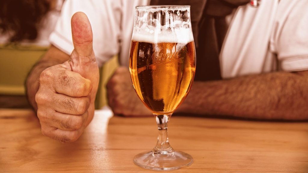 Copa de cerveza en la mesa y señor con pulgar hacia arriba